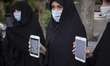 Iranian veiled women hold their smartphones with images of Koran on their smartphone’s scr...