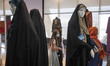 Two Iranian young girls and their mother walk past mannequins that are decorated with trad...
