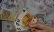 A person holds banknotes of the Euro in front of a board showing the selling and buying ra...