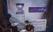 An Iranian couple eat donated meal as they sit in front of a banner with an image of the I...