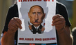 A protester holds a poster with an image of Russian President, Vladimir Putin and words 'H...