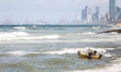 Children use a makeshift boat to play on the waves, the backdrop being the port city of Co...