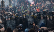 Police officers and CRS riot police officers face protesters as they stand guard during a...