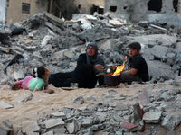 Palestinians make tea on an open fire as they sit outside a house which was destroyed by Israeli air strikes during recent fighting between...