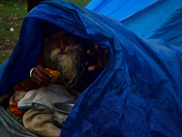 An indian roadside begger takes some eatable as he covers himself with a plastic sheet  during a cold and rainy day in Allahabad on January...