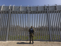 Border police officers stands in front of the fence searching for illegal entry. Greek border police officers patrol along the steel fence n...
