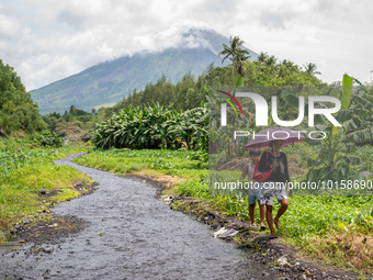 People walk past a river near the Mayon Volcano which remains under alert level 3, in Legazpi, Albay province, Philippines, on June 12, 2023...