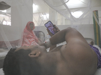 A dengue-infected patient stays under mosquito nets as he makes a video call during his treatment in the Shaheed Suhrawardy Medical College...