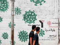  Palestinians walk past street art showing a Covid-19 coronavirus in Gaza City, on August 14, 2023. The number of new Covid-19 cases reporte...