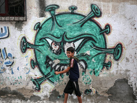 A Palestinian boy walks past street art showing a Covid-19 coronavirus in Gaza City, on August 14, 2023. The number of new Covid-19 cases re...