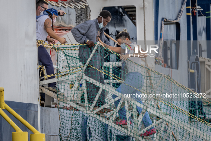 A volunteer helps a migrant to disembark from MSF's (Doctors Without Borders) Geo Barents ship at the Italian port of Brindisi on September...