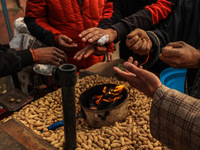 Kashmiri men are warming their hands while a vendor is selling roasted groundnuts from his cart on a cold winter morning in Sopore District,...