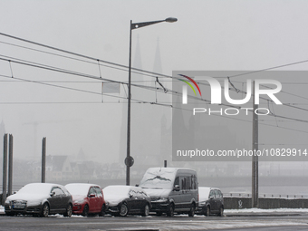 Cars are parked as the Cologne Cathedral is visible in the background in Cologne, Germany, on December 4, 2023, while snow continues to fall...