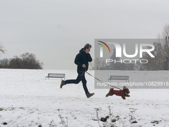 A man is running with his dog at Nagasaki Hiroshima Park in Cologne, Germany, on December 4, 2023, as snow continues to fall on Cologne. (