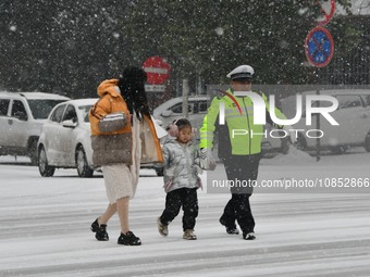 Traffic police are escorting children and parents across the road in the snow in Handan, Hebei Province, China, on December 14, 2023. (