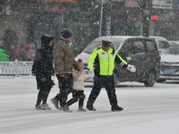 Traffic police are escorting children and parents across the road in the snow in Handan, Hebei Province, China, on December 14, 2023. (