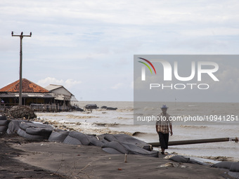 Carmat (83) is walking on the beach near the remains of his house, which was destroyed by high waves in Cemarajaya Village, Karawang Regency...
