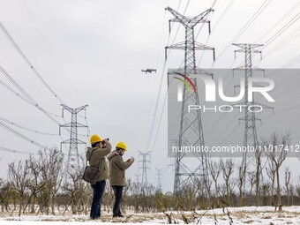 A staff member of a power supply company is using a drone to inspect the ice covering on power lines in Taizhou, Jiangsu Province, China, on...