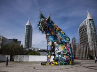 Several people are walking near a statue representing an Iberian lynx in the vicinity of Das Nacoes Park, located in the eastern district of...