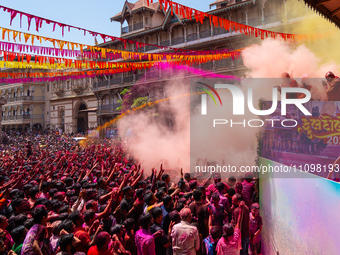 Thousands of devotees are cheering as a priest sprays colored powder and water on them during the celebrations of the colorful Holi festival...