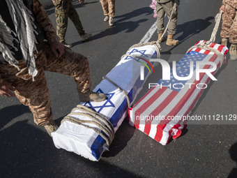 A member of the Islamic Revolutionary Guard Corps (IRGC) is placing his foot on an Israeli flag that covers a coffin symbolizing the death o...