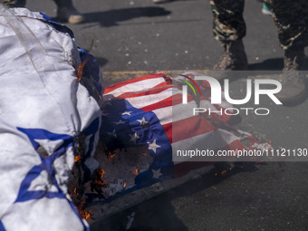 A member of the Islamic Revolutionary Guard Corps (IRGC) is standing next to burning Israeli and U.S. flags during a funeral for members of...
