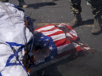 A member of the Islamic Revolutionary Guard Corps (IRGC) is standing next to burning Israeli and U.S. flags during a funeral for members of...
