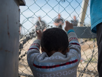 Child touching the fence of the Macedonian border. Macedonian police behind it. In Idomeni camp on April 6, 2016. (