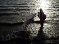 An indian woman washes her saree after taking a holy dip in Yamuna river, in a heavy dust strom and killer heat waves , during a hot day in...