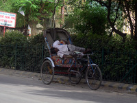 An indian rickshaw puller takes a nap in his rickshaw on the side fringes of a busy road,  in a heavy dust strom and killer heat waves , dur...