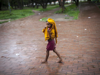 A homeless child walking in a park cover her head with a yellow cloth to save from rain water in Dhaka, Bangladesh on May 24, 2016. (