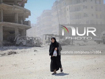 A Syrian woman walks amid rubble of what activists said it was a barrel-bomb by aircraft loyal to Syria's president Bashar al-Assad on Qadi...