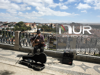 A street musician plays fados in the viewpoint of Sao Pedro Alcantara with the city of Lisbon in the background.
 (