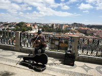 A street musician plays fados in the viewpoint of Sao Pedro Alcantara with the city of Lisbon in the background.
 (