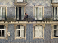 A young woman chatting with her smartphone on a balcony in the area of the upper district of Lisbon with the decoration of typical Portugues...