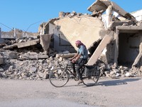 A Syrian man rides a bike past destroyed buildings in the rebel-held town of Douma, on the eastern outskirts of the Syrian capital Damascus,...