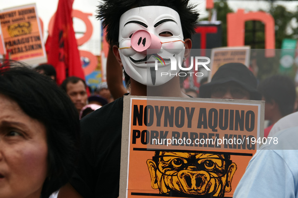 A protester wearing a Guy Fawkes mask with a pig's nose while holding a poster of President Aquino III. Thousands of protesters rallied at t...