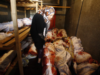 A Palestinian relatives stand among bodies in a stored vegetable refrigerator in Rafah, in the southern Gaza Strip on August 2, 2014. A fres...