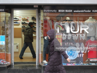 People walking in opposite directions. A male is inside the Urban Menswear store as a female passes the outside store. (