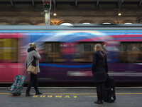 A train arriving at Preston station as two people wait on the platform. (
