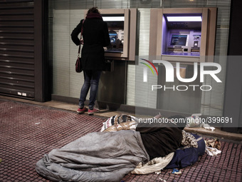 A homeless man lies on the pavement in front of a bank while a woman withdraws money from the ATM in Athens on January 18, 2015. (