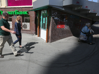 People walk past the entrance of the branch of Privat Bank while another woman at right asks for money from passers-by in Kyiv, Ukraine, Apr...