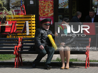 A man wearing military officer uniform talk to a woman sitting on a bench at Khreshchatyk street as warm spring weather comes in Kyiv, Ukrai...