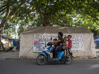 Disaster survivors riding motorbikes crossed near emergency tents with banners filled with demands for payment of Life Security funds (Jadup...