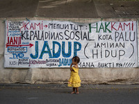A child survivor of a disaster stands near a makeshift tent with a banner containing demands for payment of the Life Insurance fund (Jadup)...
