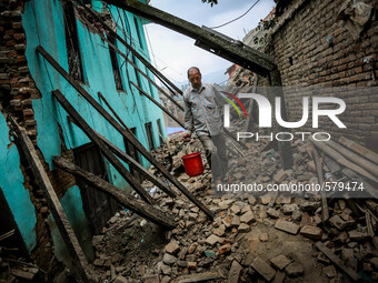 A man is carrying a bucket of water through a road of rubbles beside a destroyed bulding. Sankhu, Nepal. May 9, 2015. (