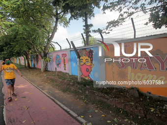 Commuters are seen on the road as they walks past near to the awareness wall painting about COVID-19 coronavirus done by state government fo...