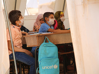 Syrian students wearing protective masks sit on their seats during the first day of the school year in a camp for displaced people near the...