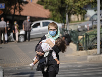 An Iranian woman wearing a protective face mask carrying her kid as she crosses an avenue. in northern Tehran while the new coronavirus (COV...