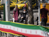 An Iranian woman wearing a protective face mask walks along an avenue in northern Tehran while the new coronavirus (COVID-19) disease rapid...
